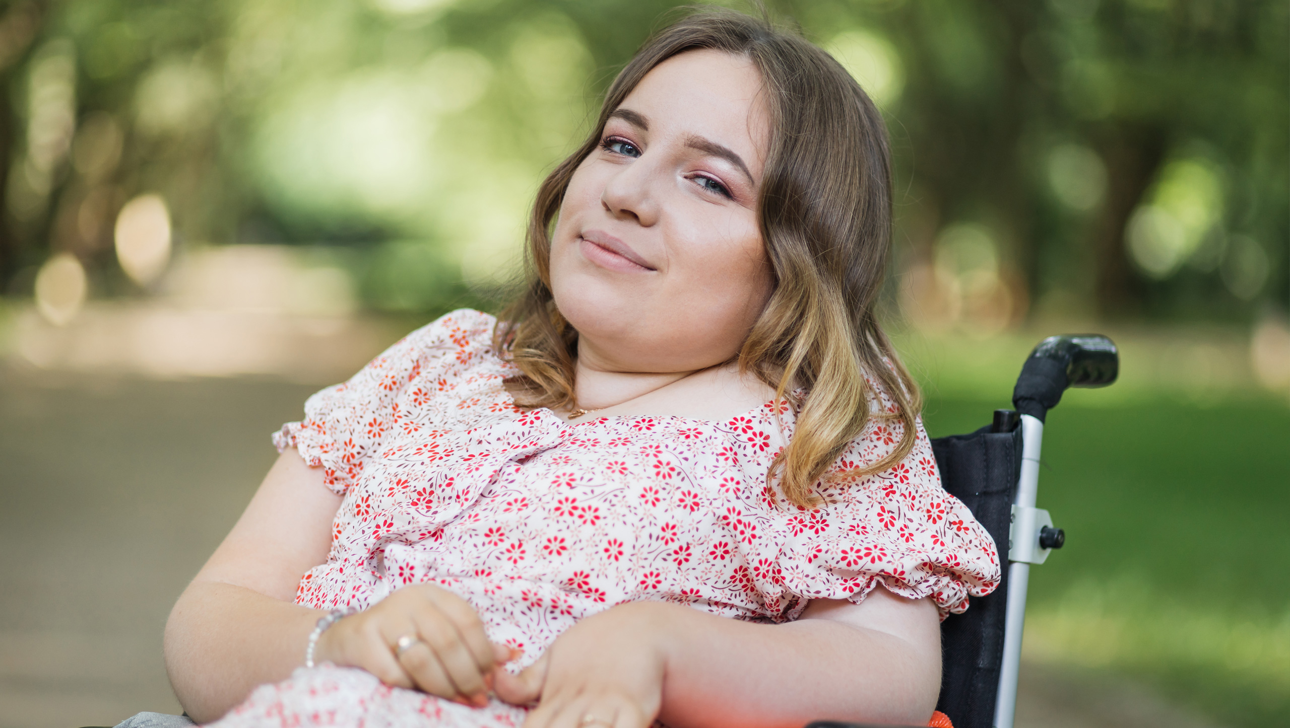 A girl sitting on a wheelchair, smiling and looking towards the camera.
